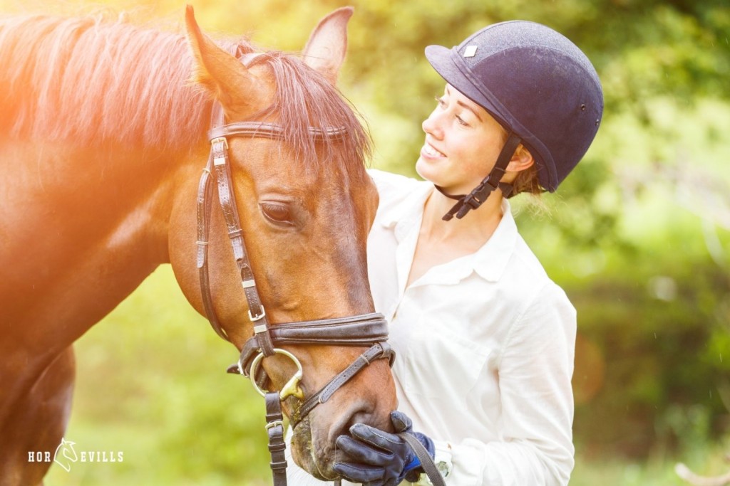 lady wearing a horse riding a helmet touching her horse