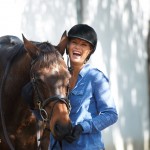 A lady next to a horse laughing